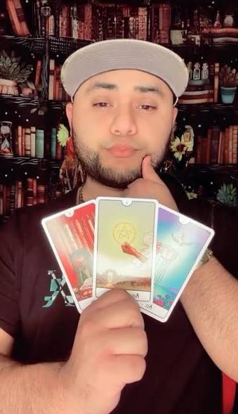 Fotografía original de Roberto Rodríguez sosteniendo tres cartas de tarot frente a una biblioteca